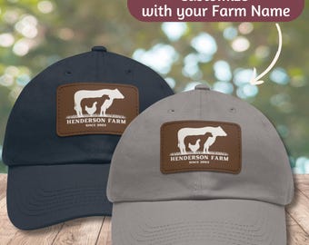 May include: Two baseball caps with a brown leather patch featuring a cow and a chicken silhouette. The text on the patch reads "Henderson Farm Since 2003". One cap is navy blue and the other is gray.