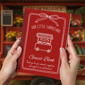 May include: A red spiral-bound guest book with white text and illustrations. The cover reads "Our Little Farmstand Guest Book" with a drawing of a farm stand. The text also includes a thank you message for comments and support.