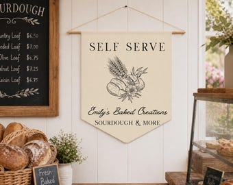 May include: A cream-colored banner with the words "SELF SERVE" and "Emily's Baked Creations" in black lettering. The banner features a bread and wheat illustration. A chalkboard menu and a basket of bread are also visible.