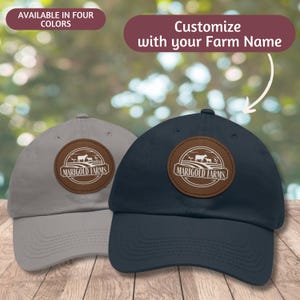 May include: Two baseball caps with a brown leather patch featuring a farm scene and the text "Marigold Farms". One cap is grey and the other is navy blue.