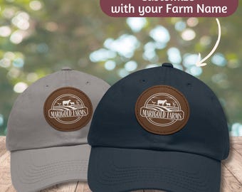 May include: Two baseball caps with a brown leather patch featuring a farm scene and the text "Marigold Farms". One cap is gray and the other is navy blue.