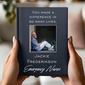 May include: A dark blue book with the text "You Made a Difference in So Many Lives." A photo of a woman in a blue shirt and white pants is in the center. The name "Jackie Frederikson" and the title "Emergency Nurse" are below the photo.