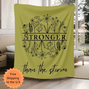 Könnte beinhalten: Ein senfgelber Wandteppich mit einem schwarzen Blumendesign und dem Text "Stronger than the storm".