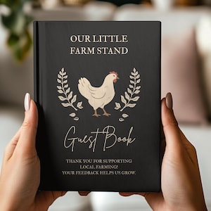 May include: A black hardcover guest book featuring the text OUR LITTLE FARM STAND at the top, a central illustration of a cream-colored chicken flanked by two wheat stalks, the words Guest Book below, and text thanking customers for supporting local farming.
