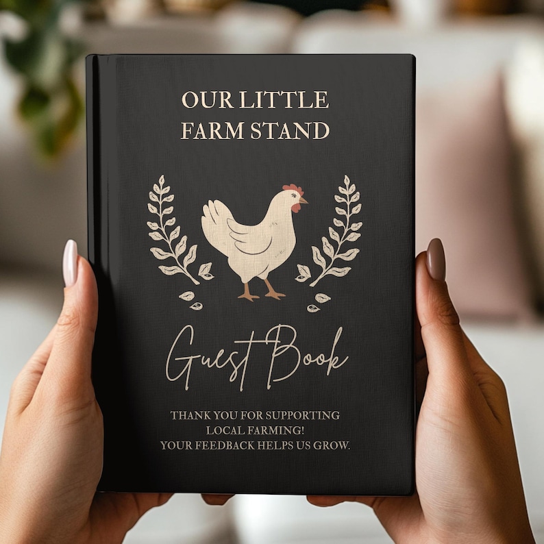 May include: A black hardcover guest book featuring the text OUR LITTLE FARM STAND at the top, a central illustration of a cream-colored chicken flanked by two wheat stalks, the words Guest Book below, and text thanking customers for supporting local farming.