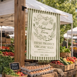 以下が含まれることがあります： 「Maplewood Farms Fresh Produce Organic Eggs」と書かれた看板があるファーマーズマーケットのシーン。看板には緑と白のストライプのボーダーがあり、野菜と卵のイラストが描かれています。新鮮な農産物と卵のカートンが展示されています。