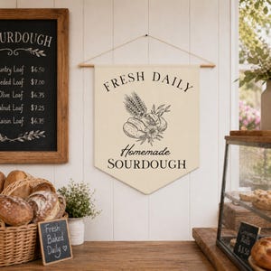 May include: A beige banner with the words "FRESH DAILY Homemade SOURDOUGH" in black script. The banner features a bread and floral illustration. A chalkboard menu lists sourdough bread varieties and prices. Baskets of bread and a small sign that says "Fresh Baked Daily" are also visible.