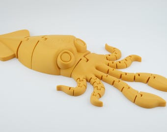 Puede incluir: Un juguete de pulpo articulado, impreso en 3D, de color amarillo mostaza. El pulpo tiene un cuerpo y tentáculos segmentados, con ojos grandes y circulares. El juguete está diseñado para ser articulado y está sobre una superficie blanca.
