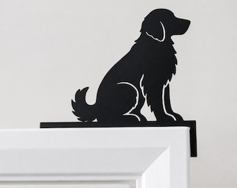 Puede incluir: Una silueta de metal negro mate de un perro sentado con pelo largo, diseñada como un adorno decorativo para colocar en la esquina superior del marco de una puerta. El recorte plano y negro muestra el perfil distintivo de un canino.