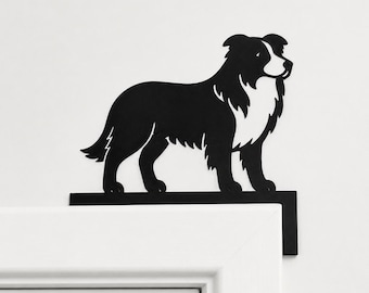 Puede incluir: Una silueta de metal negro de un perro Border Collie de pie de perfil. La figura presenta un área blanca en el pecho y la cara, y está montada sobre un soporte plano en forma de L diseñado para descansar sobre la esquina superior del marco de una puerta.