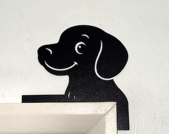 May include: Black metal dog silhouette decoration. The dog is smiling and appears to be peeking over a door frame. The dog's head and body are black, with white accents for the eye and ear.