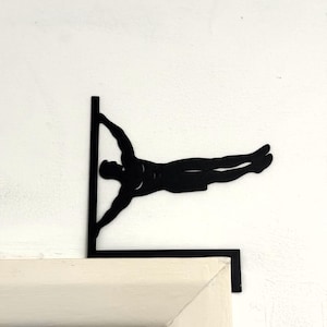 Peut inclure: Décoration murale en métal noir représentant un gymnaste en position du drapeau. La silhouette est montée sur un coin, le corps du gymnaste parallèle au mur. La pièce est conçue pour être fixée sur un mur ou un cadre de porte.