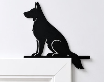 Puede incluir: Una silueta de metal negro de un perro pastor alemán sentado, diseñada para montarse en la esquina superior del marco de una puerta. El perro se muestra de perfil con orejas puntiagudas y una cola larga que sobresale del borde del marco.