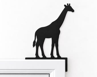 Puede incluir: Un adorno para puerta de metal negro mate con la silueta de una jirafa de pie sobre una base horizontal plana. El soporte en forma de L está diseñado para descansar sobre la esquina superior del marco de una puerta.