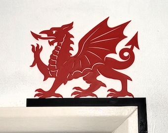 Puede incluir: Un emblema de dragón rojo, símbolo de Gales, con alas extendidas y cola enroscada. Montado sobre una base negra, sobre un marco de puerta blanco.