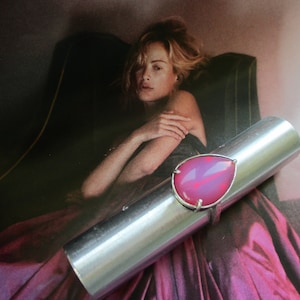 May include: A silver ring with a large pink teardrop-shaped gemstone. The ring is on a silver tube.
