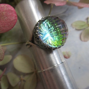 May include: A silver ring with a large, round, iridescent green glass stone set in a decorative silver bezel.