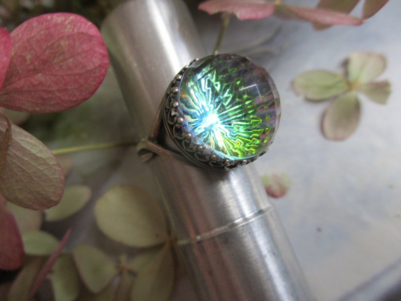May include: A silver ring with a large, round, iridescent green glass stone set in a decorative silver bezel.