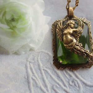 K&ouml;nnte beinhalten: Eine goldene Halskette mit einem gr&uuml;nen Glas-Cameo, das eine Meerjungfrau mit Fischschwanz und Fl&uuml;geln zeigt. Der Cameo ist in einen goldenen Rahmen mit verzierten Details gefasst.