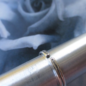 May include: A silver ring with a smooth, polished finish. The ring is on a silver cylinder.