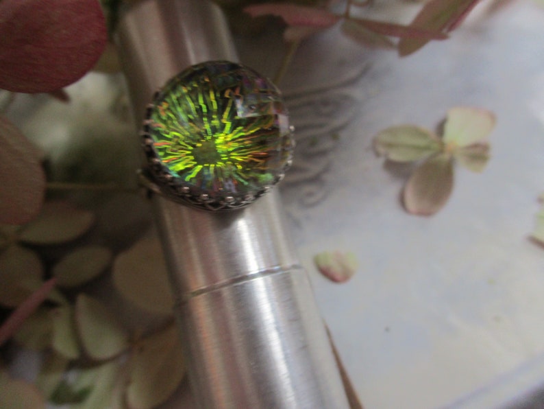 May include: A silver ring with a large oval-shaped iridescent gemstone. The gemstone has a green, yellow, and blue color with a starburst pattern.