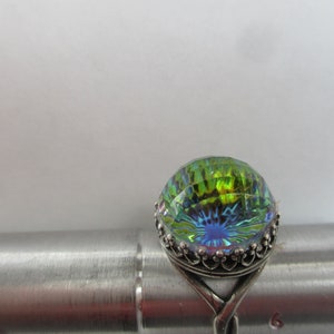 May include: A silver ring with a large iridescent green and blue gemstone. The gemstone is faceted and has a starburst pattern.