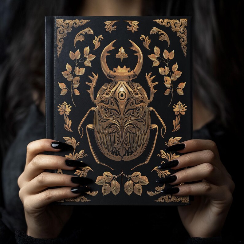 May include: A black hardcover journal with a gold beetle design. The beetle is intricately detailed with ornate patterns and a single eye in the center. The background is black with gold floral accents.