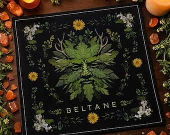 May include: Black square altar cloth featuring a Green Man design made of leaves, antlers, and a face. The cloth is bordered with white stitching and has the word "BELTANE" printed in white. Yellow flowers and white blossoms surround the central image.