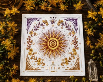 May include: Square white cloth with a sun design at the center, surrounded by floral and bee illustrations. The word "LITHA" is printed below the sun. The design features gold, purple, and brown colors.