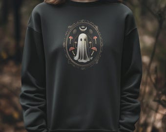 May include: Dark gray sweatshirt featuring a framed illustration of a ghost with mushrooms and a crescent moon. The ghost is white with two black eyes. The frame is gold with a decorative border. The mushrooms are red and white.
