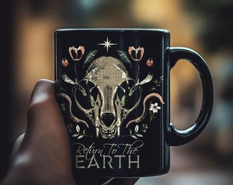 May include: Black ceramic mug featuring a detailed illustration of a skull with floral and botanical elements. The design includes a star, ladybugs, and the text "Return To The Earth" in a decorative font. The mug has a black handle and a glossy finish.