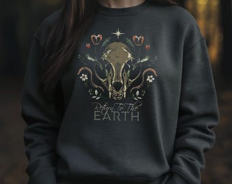 May include: Dark gray sweatshirt featuring a detailed graphic of a skull surrounded by flowers and foliage. The design includes the text "Return to the Earth" in a stylized font. The overall aesthetic is nature-inspired and artistic.