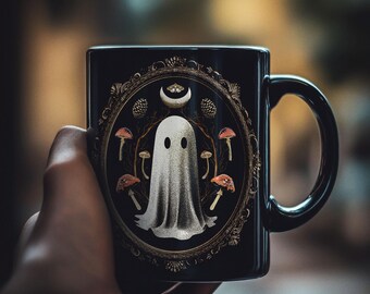 May include: Black ceramic mug featuring a white ghost illustration within a decorative frame. The frame includes mushrooms, pinecones, and a crescent moon. The mug has a black handle and a glossy finish, perfect for Halloween.