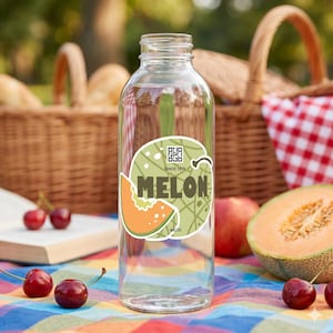 May include: A clear glass bottle with a green and orange melon sticker. The sticker reads "MELON" with a melon slice graphic. The bottle is on a colorful picnic blanket with cherries and a cantaloupe half.