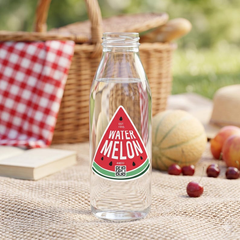 May include: A clear glass bottle with a red, white, and green watermelon label. The label reads "WATERMELON" in white text, with a QR code and the text "#4032". The bottle is filled with a clear liquid and sits on a picnic blanket.