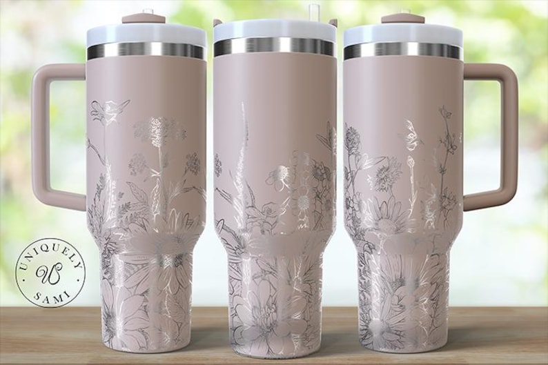 May include: Three insulated tumblers with handles, featuring a light pink finish and silver floral designs. Each tumbler has a white lid and a matching pink handle. The tumblers are displayed on a wooden surface.