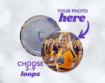 May include: A circular custom photo button featuring a smiling cheerleader in a yellow and blue uniform with the text TIGERS GGI. The design includes purple text that reads YOUR PHOTO here with an arrow and CHOOSE 3-9 loops below the image.