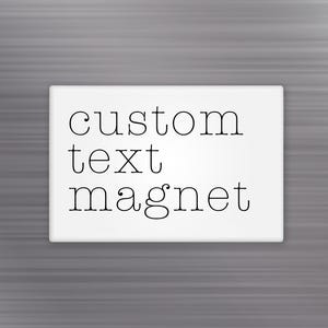 May include: A rectangular white magnet with the words "custom text magnet" in black, centered on the surface. The text is in a simple, elegant font. The background is a gray, textured surface.