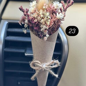 May include: A small bouquet of dried flowers in a brown paper cone, tied with twine. The flowers are a mix of white, pink, and burgundy, with a fluffy tan accent. The number "23" is in a black circle.