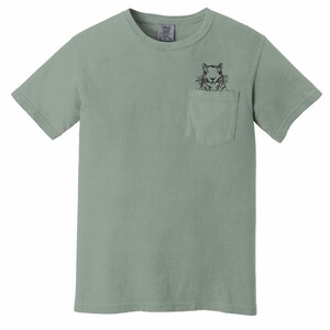 A light green t-shirt with a small black illustration of a squirrel peeking out of a pocket on the front.