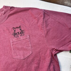 A red t-shirt with a small black illustration of a squirrel on the front pocket.