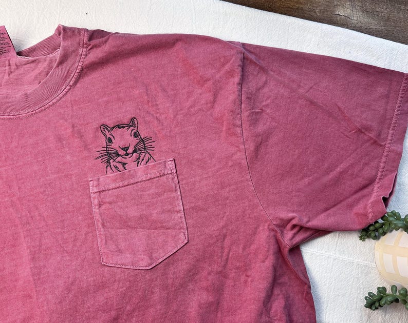 A red t-shirt with a small black illustration of a squirrel on the front pocket.