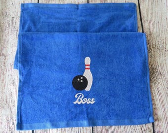 May include: A bright blue rectangular hand towel featuring an embroidered design of a black bowling ball and a white bowling pin with red stripes. Below the graphic, the word Boss is embroidered in white cursive script lettering.