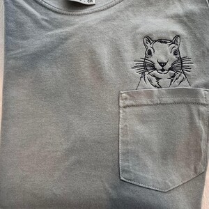 A gray t-shirt with a small black squirrel embroidered on the front pocket.