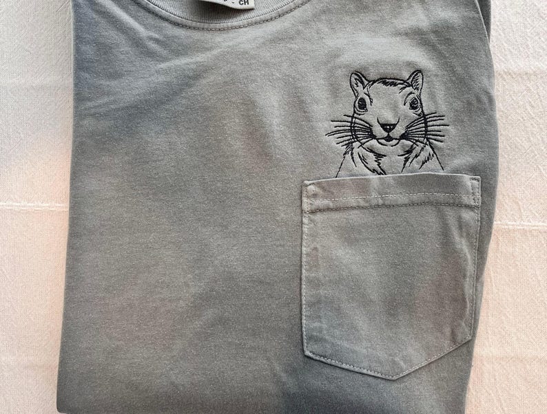 A gray t-shirt with a small black squirrel embroidered on the front pocket.