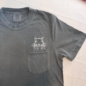 A gray t-shirt with a white embroidered image of a squirrel on the front pocket.