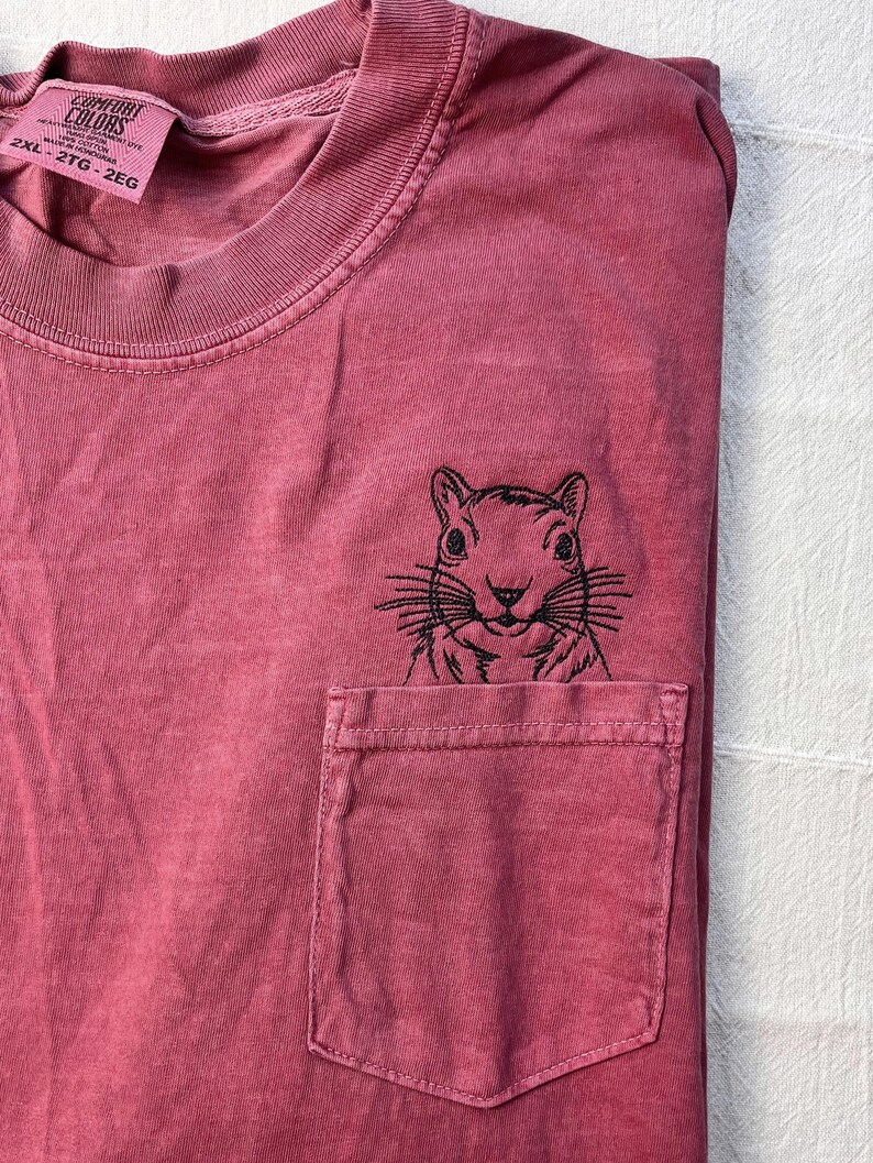 A red t-shirt with a black embroidered image of a squirrel on the front pocket.