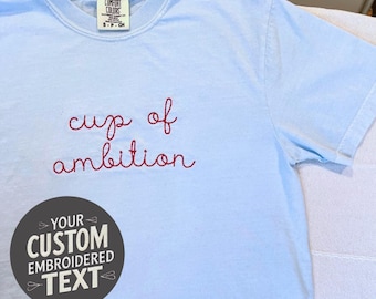 Camiseta personalizada con texto bordado en cursiva, colores cómodos y aspecto cosido a mano.