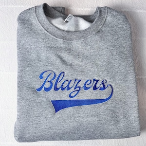 May include: A grey sweatshirt with the word "Blazers" in blue script across the front. The word has a blue tail design. The sweatshirt has a crew neck and a white interior.