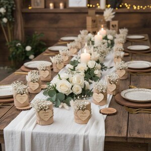 May include: A rustic wooden table set for a wedding reception. The table is adorned with white roses, candles, and small floral arrangements in cylindrical containers. Each place setting includes a plate, wooden charger, and gold cutlery.